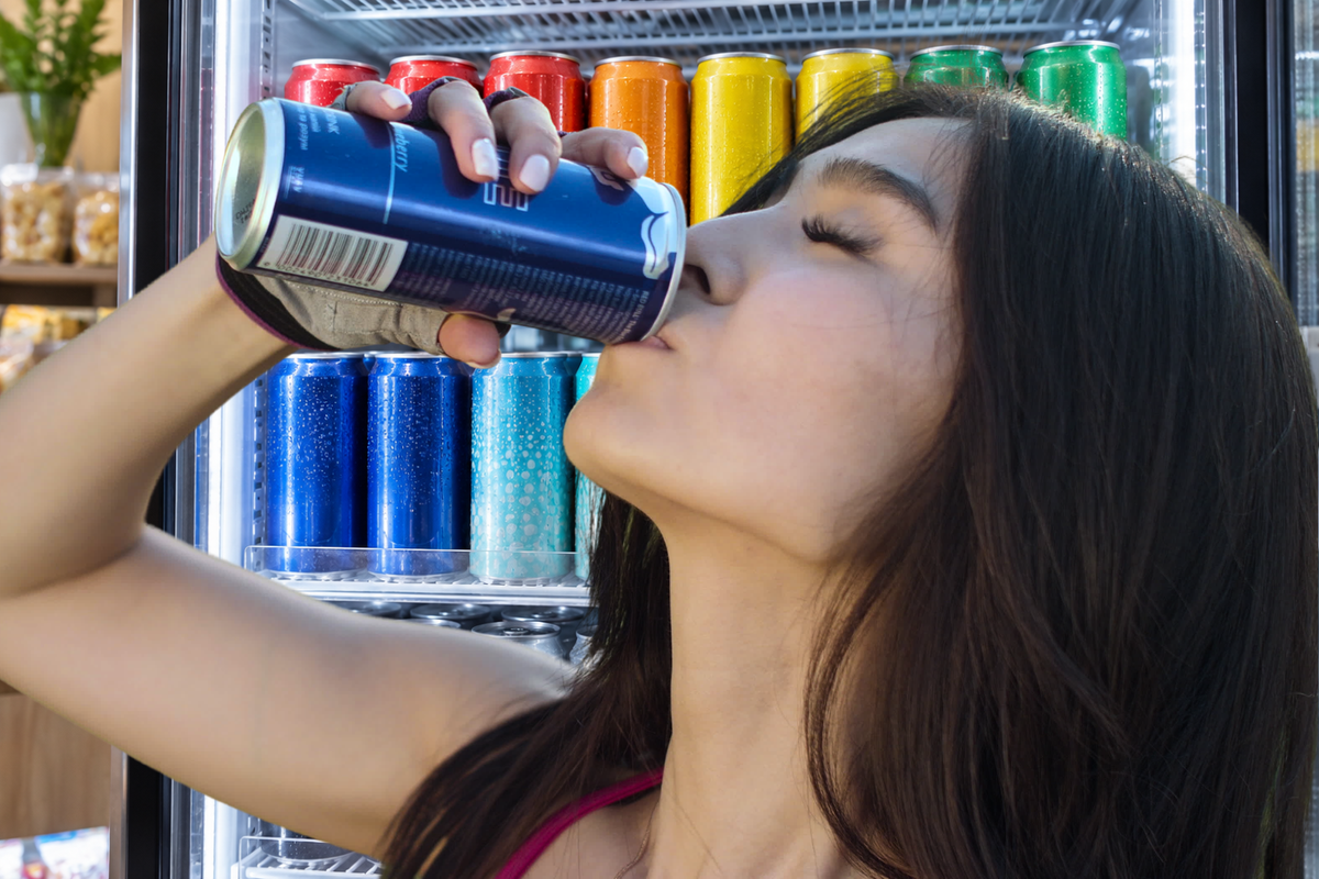 Woman drinking an energy drink in front of a chilled display, illustrating how to compare caffeine, sugar, sweeteners, and other ingredients.