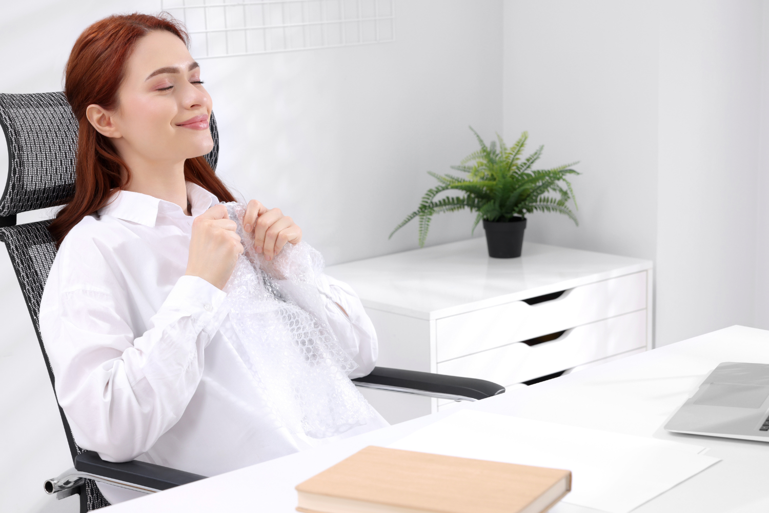 Relaxed woman sitting back at her desk with eyes closed, looking calm
