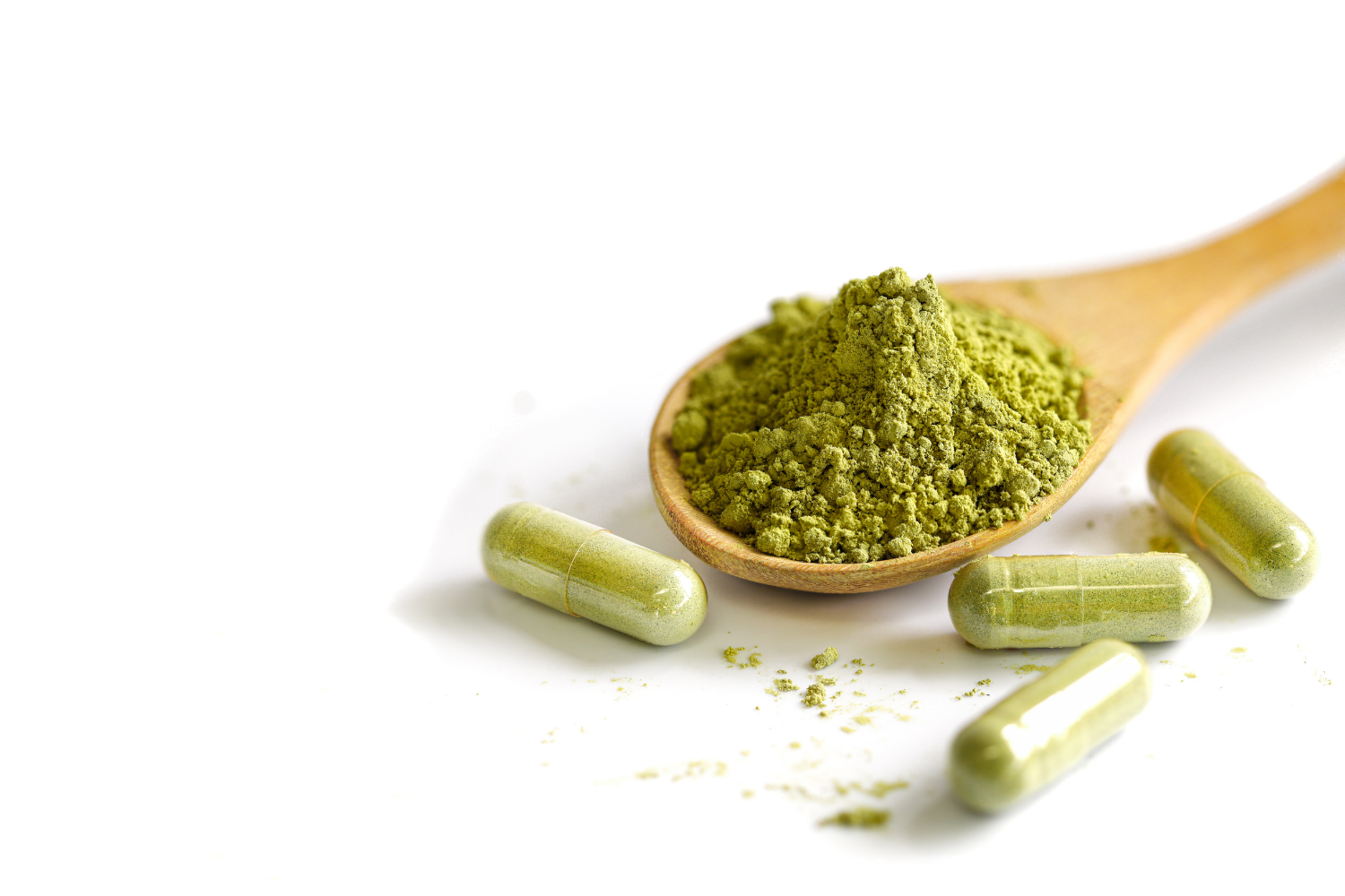 Green tea extract powder on a wooden spoon with green capsules on a white background