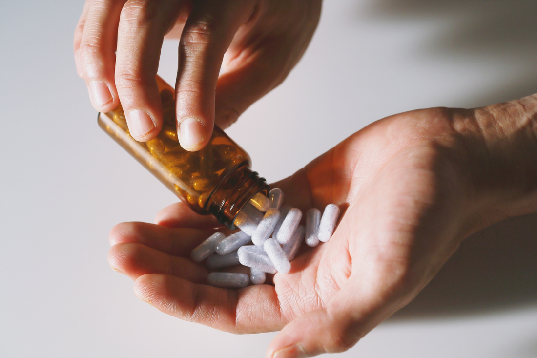Capsules being poured from a brown bottle into a hand, representing a lithium food supplement for daily trace mineral intake.