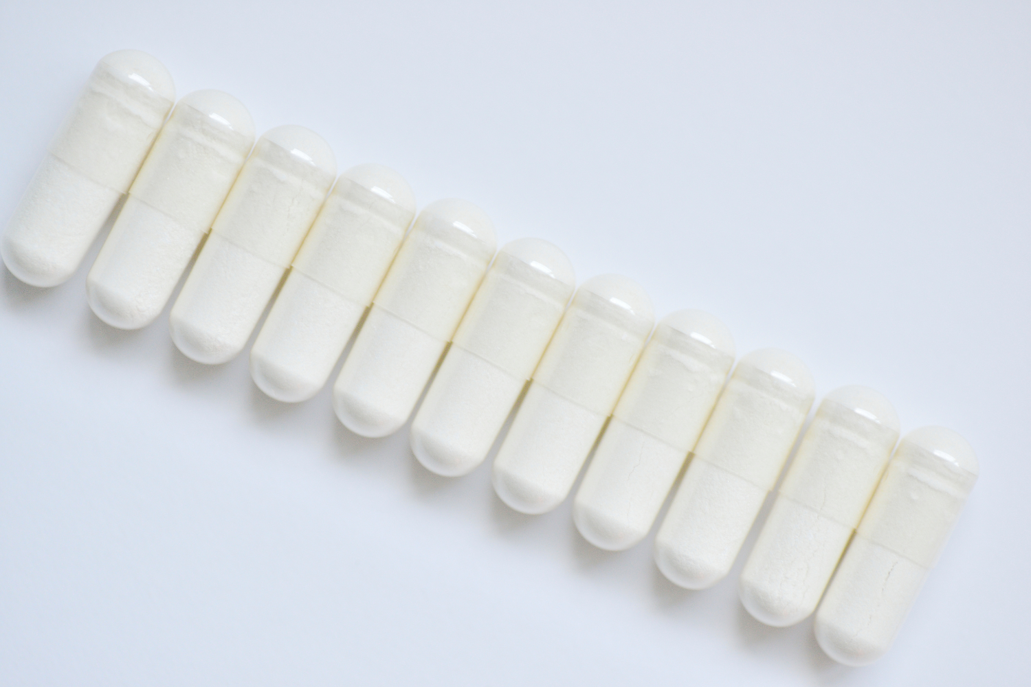 Row of white dietary supplement capsules lined up in sequence
