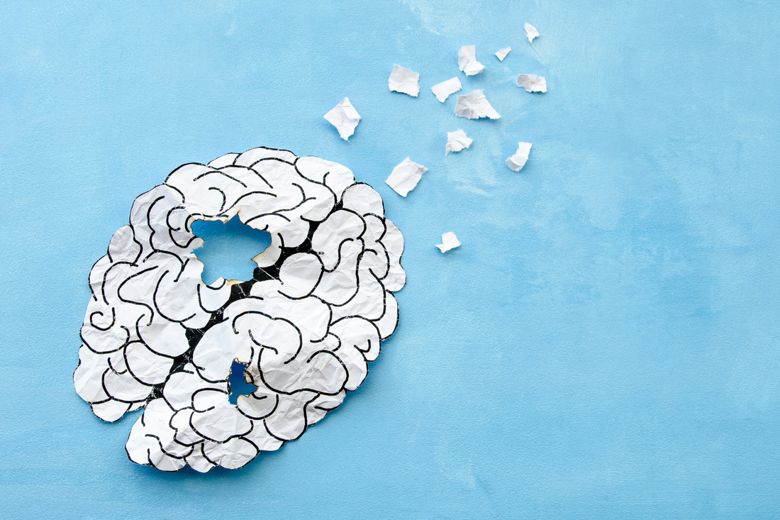 A paper cutout of a brain with pieces missing and scattered, on a blue background, signifying brain aging.