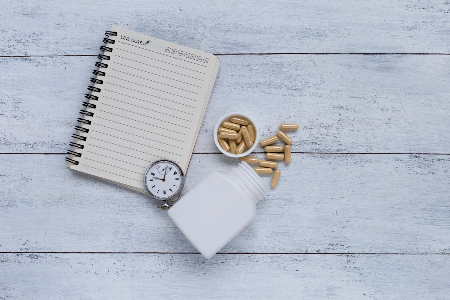 Lithium orotate capsule and bottle beside a clock and a notebook.