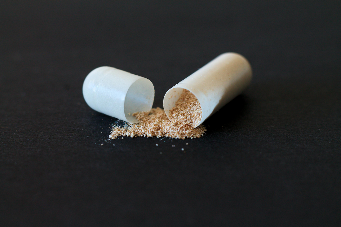 A lithium orotate capsule is split open on a black surface, with its powdery contents spilled out.