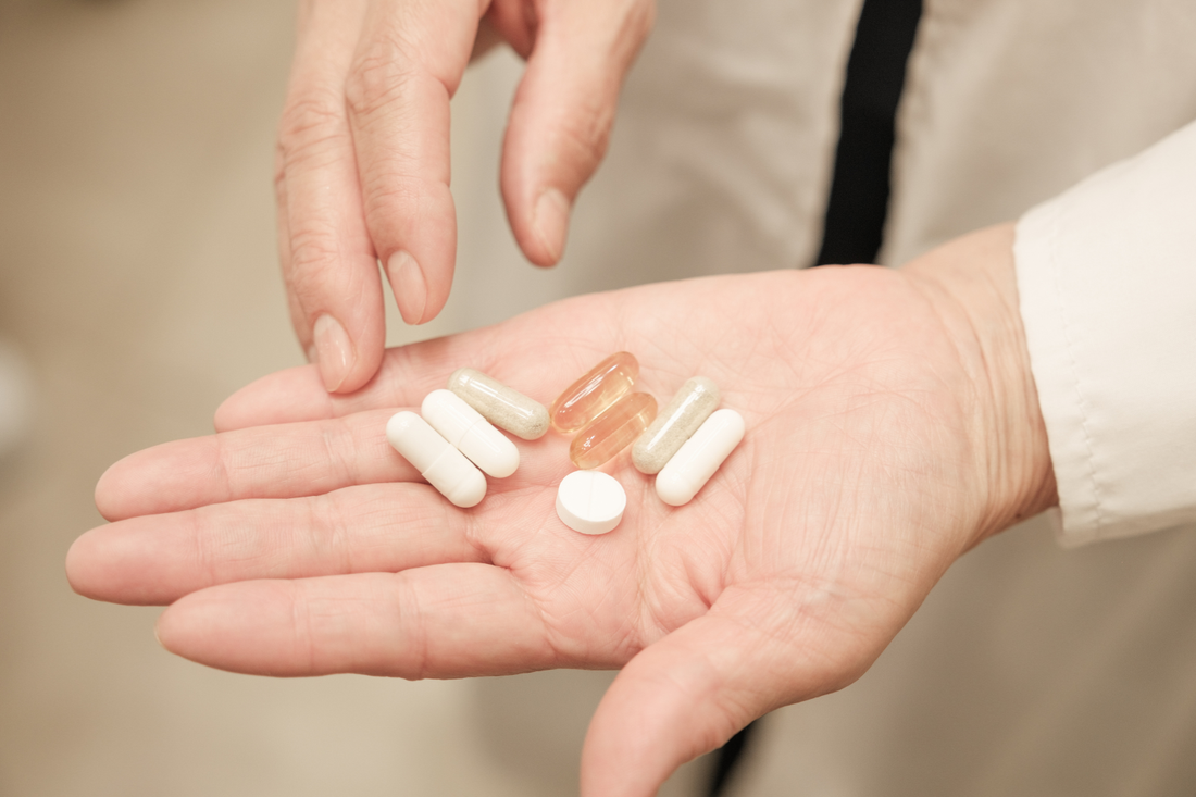 Close-up of two hands holding several white and brown capsules and a small white tablet above an open palm.