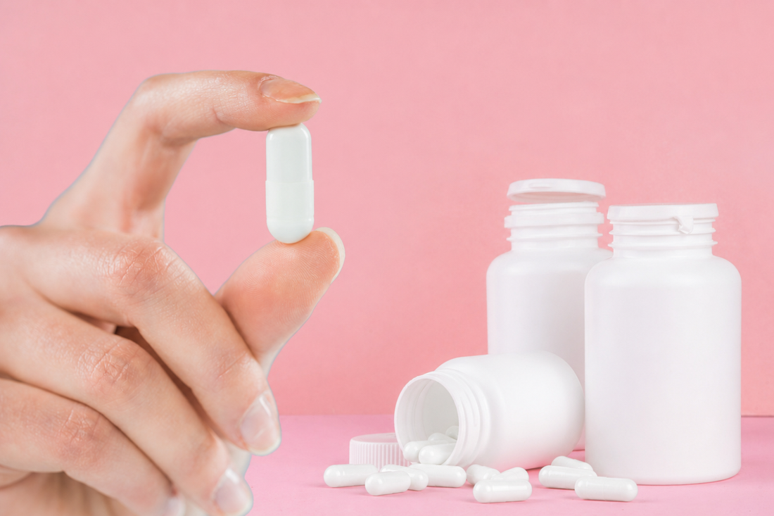 Hand holding a white capsule beside open white supplement bottles and scattered capsules.