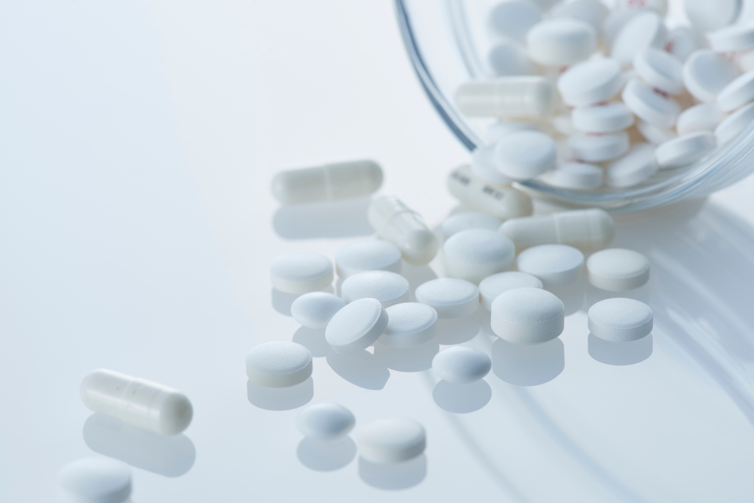 White tablets and capsules spilling from a clear glass container.