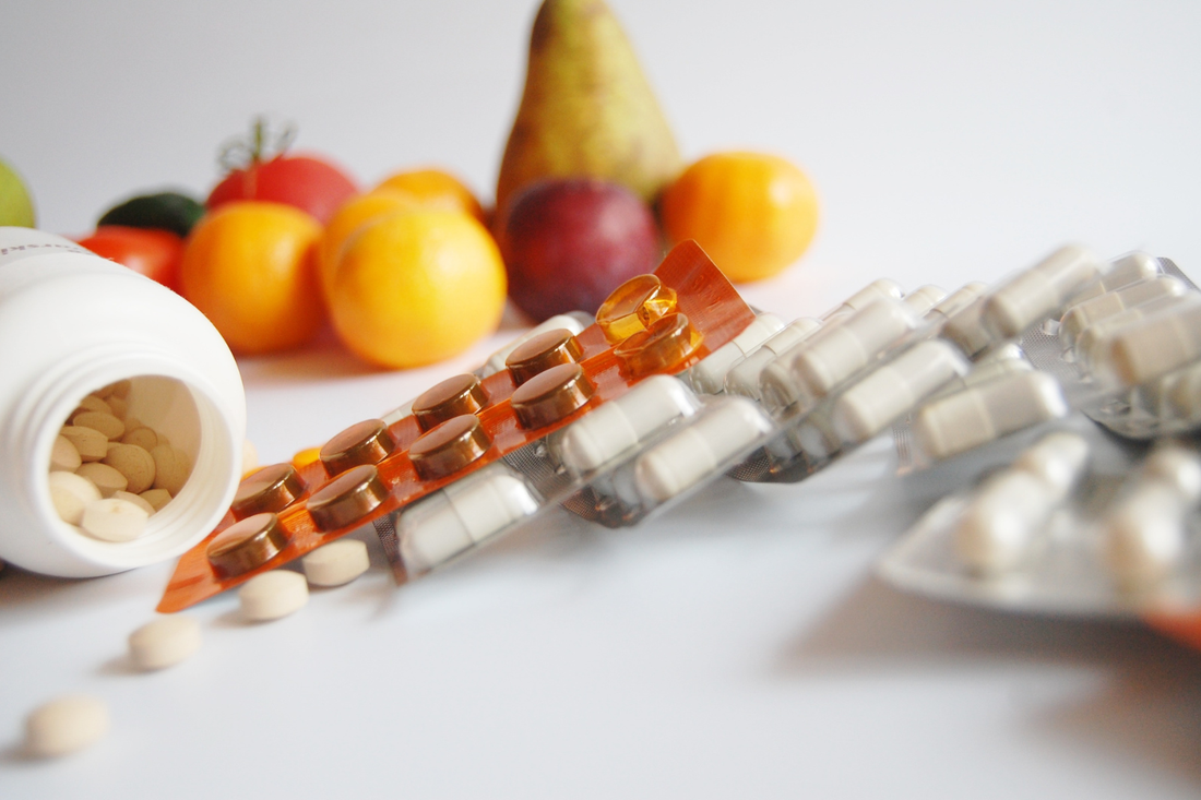 Supplement tablets and blister packs beside fresh fruit and vegetables