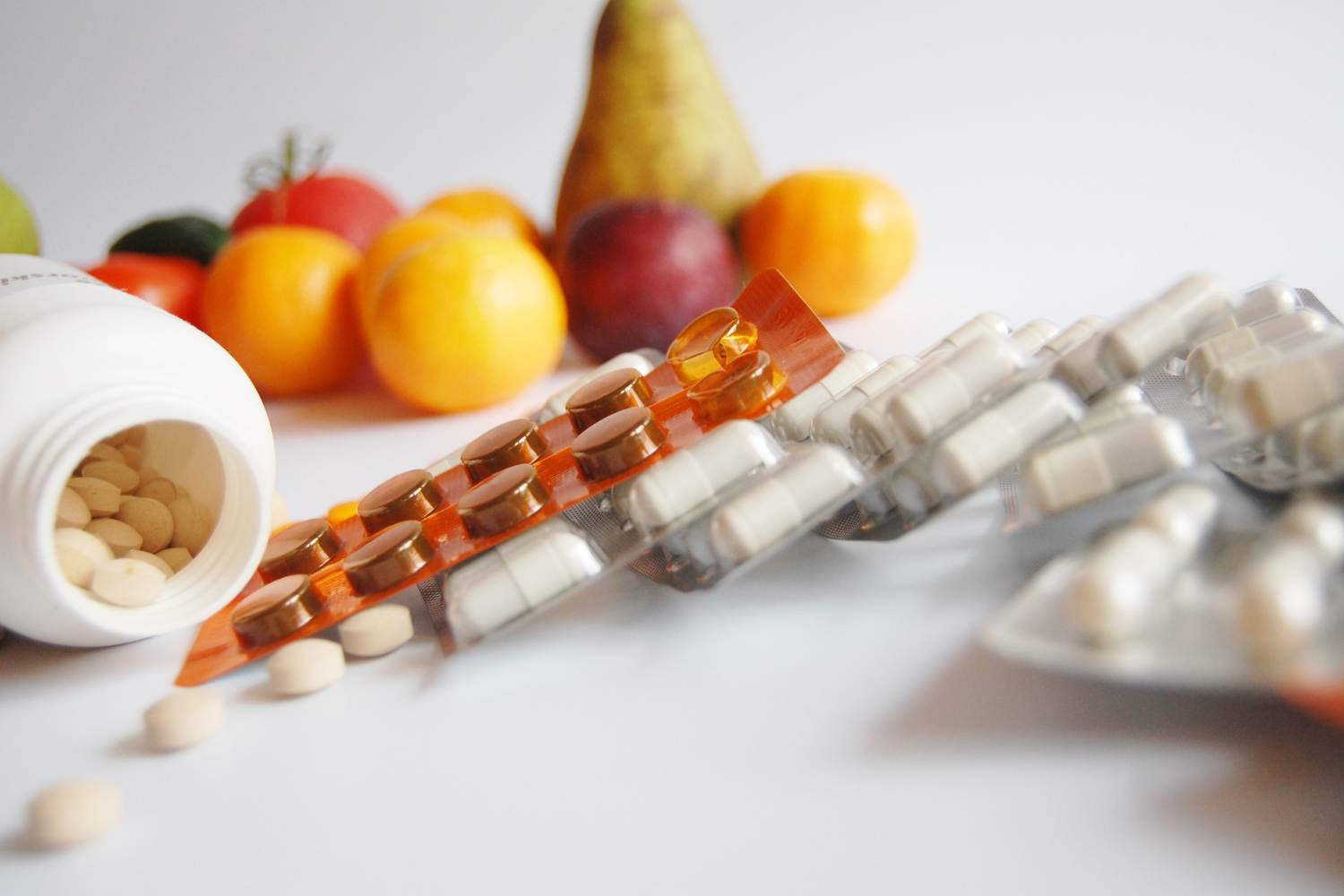 Supplement tablets and blister packs beside fresh fruit and vegetables
